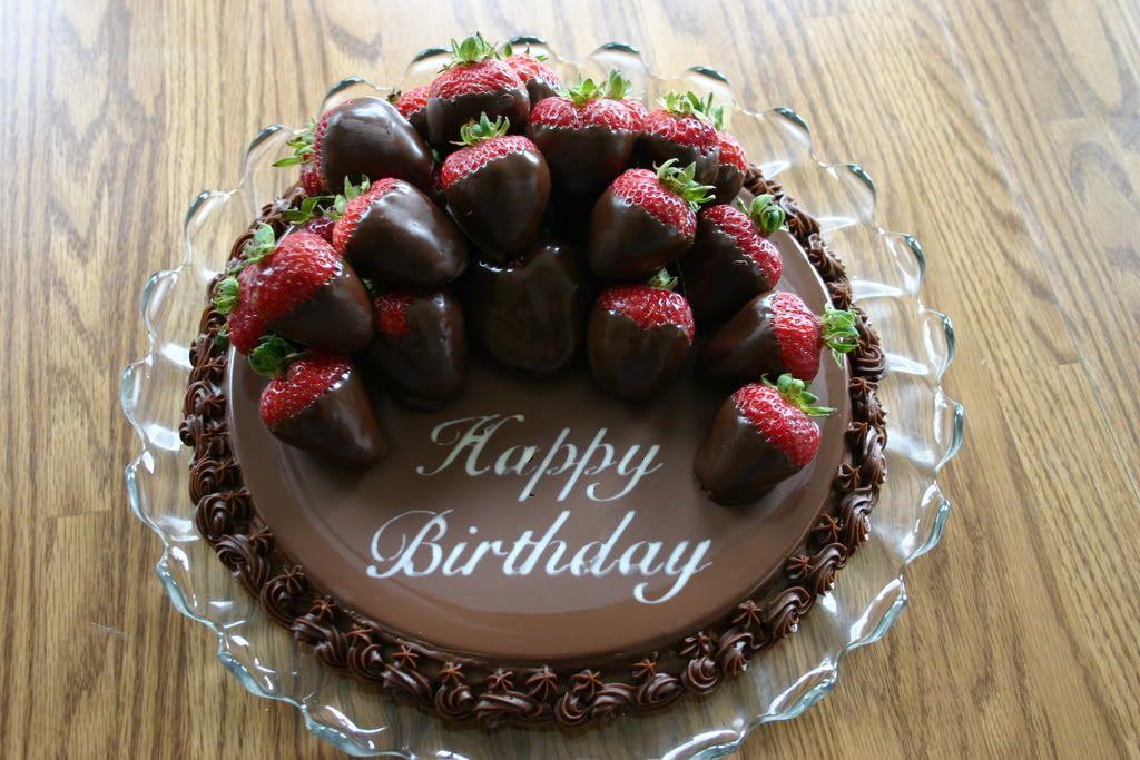 A birthday cake topped with chocolate dipped strawberries