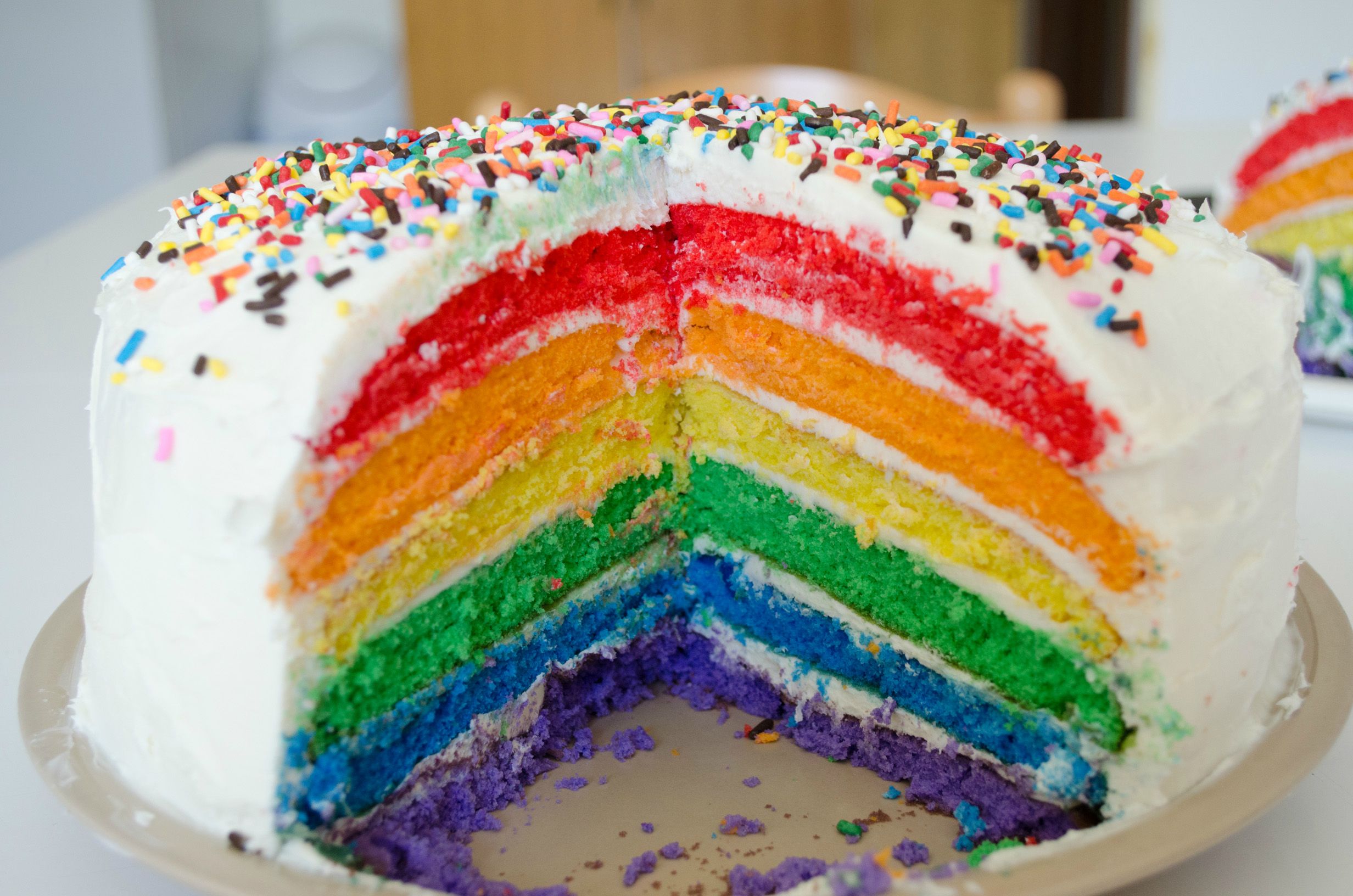 A rainbow cake coated in white buttercream and multicoloured sprinkles